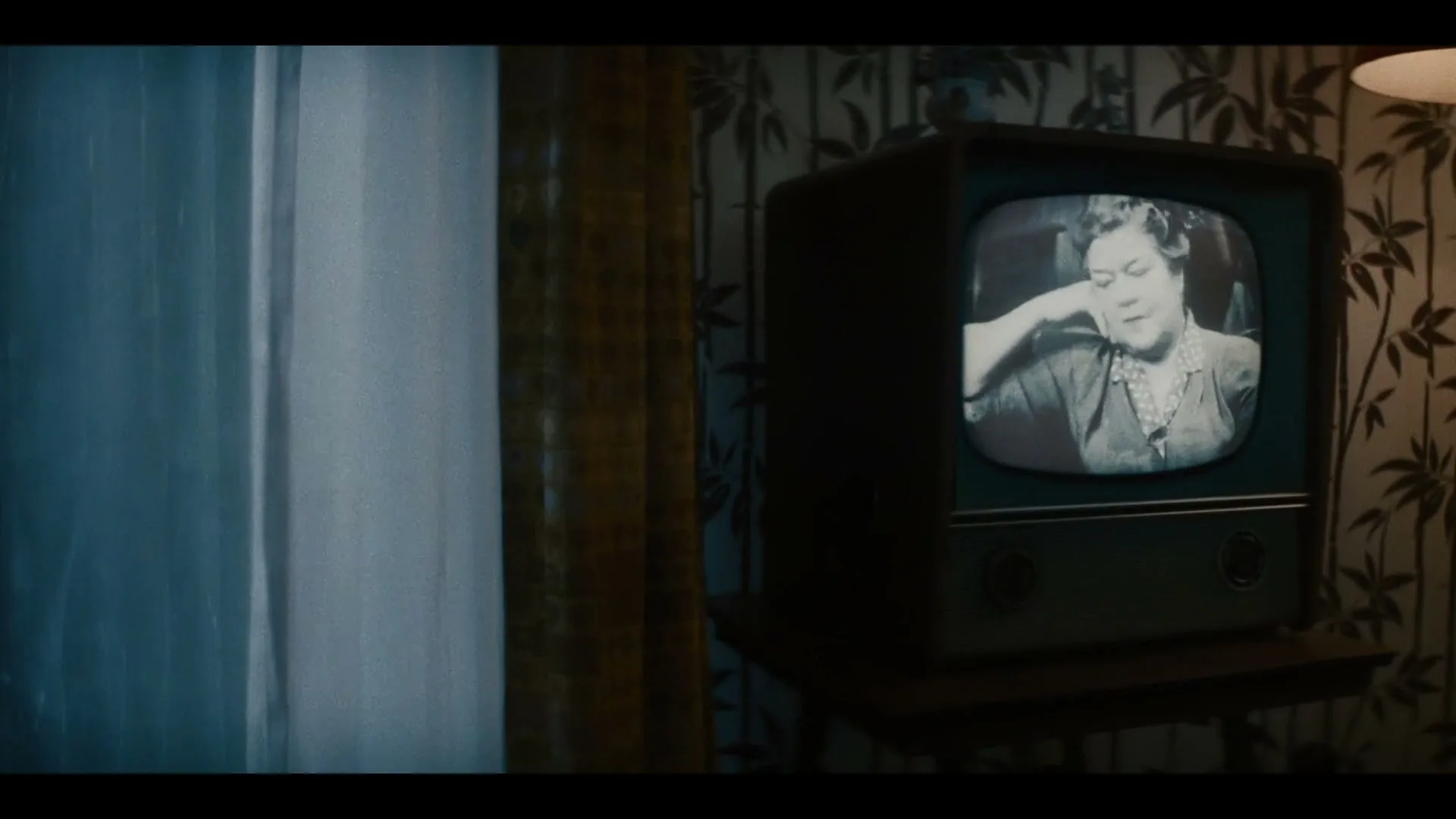 A vintage television set displays a black and white image of a woman, while a window with curtains is visible on the left.