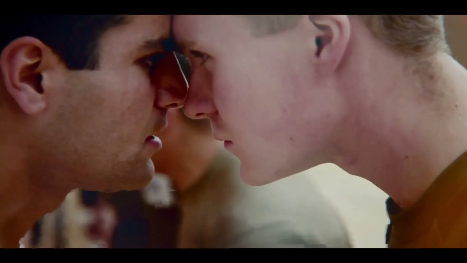 Two men, one with dark hair and one with light hair, press their foreheads together in a moment of intense connection.