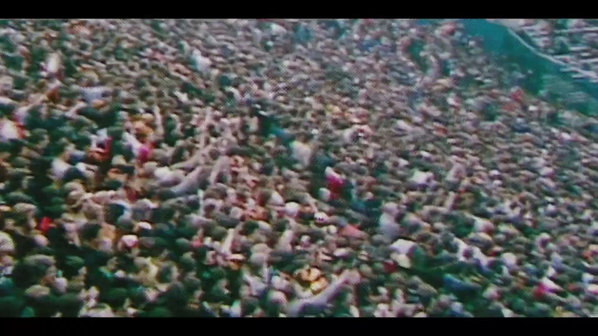 A glitchy, pixelated screen transitions to an extreme wide shot of a massive crowd of people cheering in a stadium.