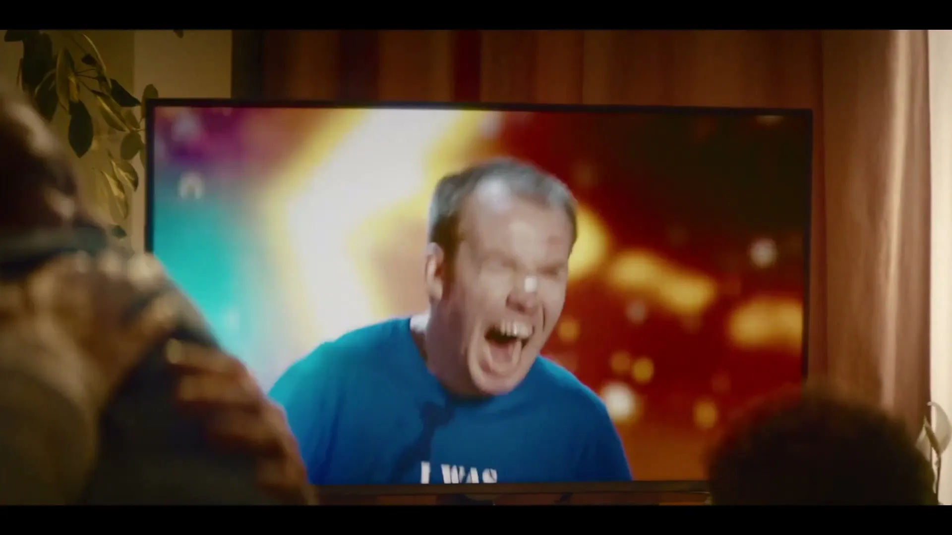 A family watches a man with a bandaged nose screaming on a television screen in their living room, with colorful lights flashing behind him.