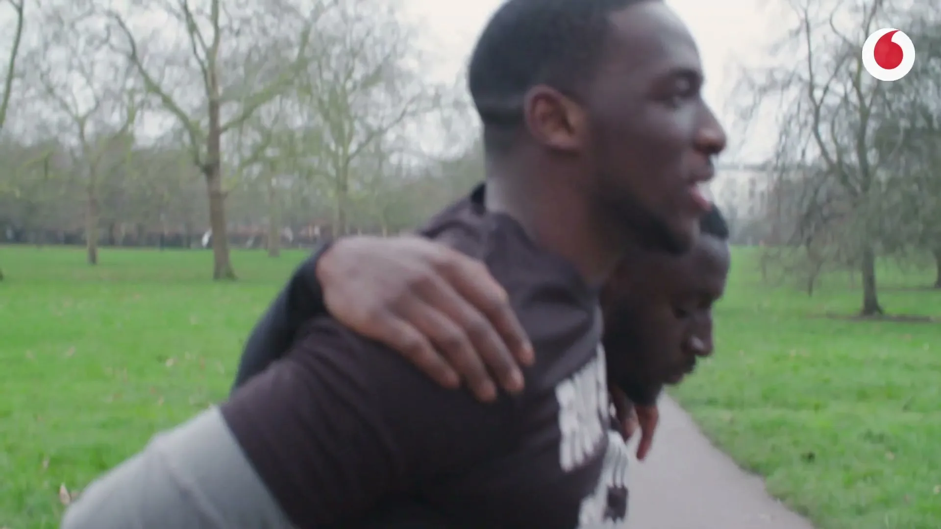 A diverse group of men in black t-shirts with "RUN WITH PURPOSE" printed on them are walking and running in a park on a cloudy day.