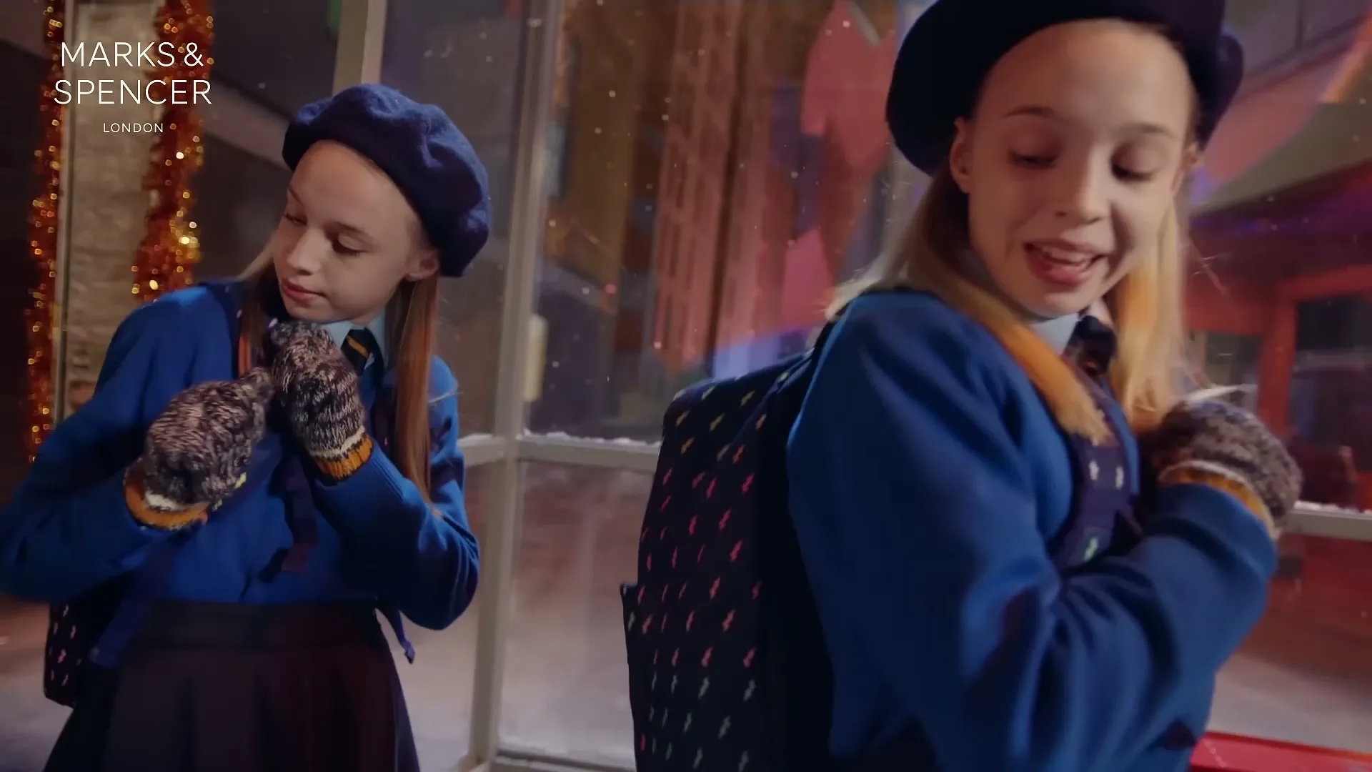 Two young girls in school uniforms and berets stand outside a window, one looking down and the other sticking out her tongue playfully.