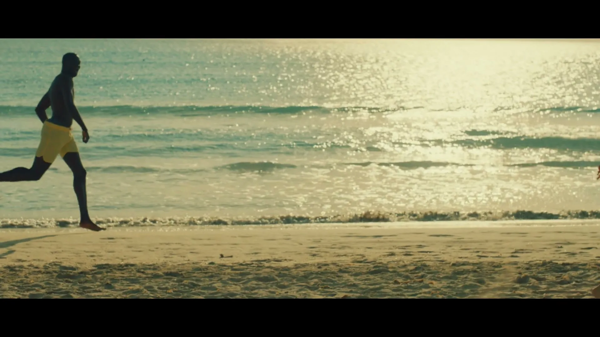 A diverse group of people of all ages and body types run joyfully along a sunny beach, with the ocean sparkling in the background.