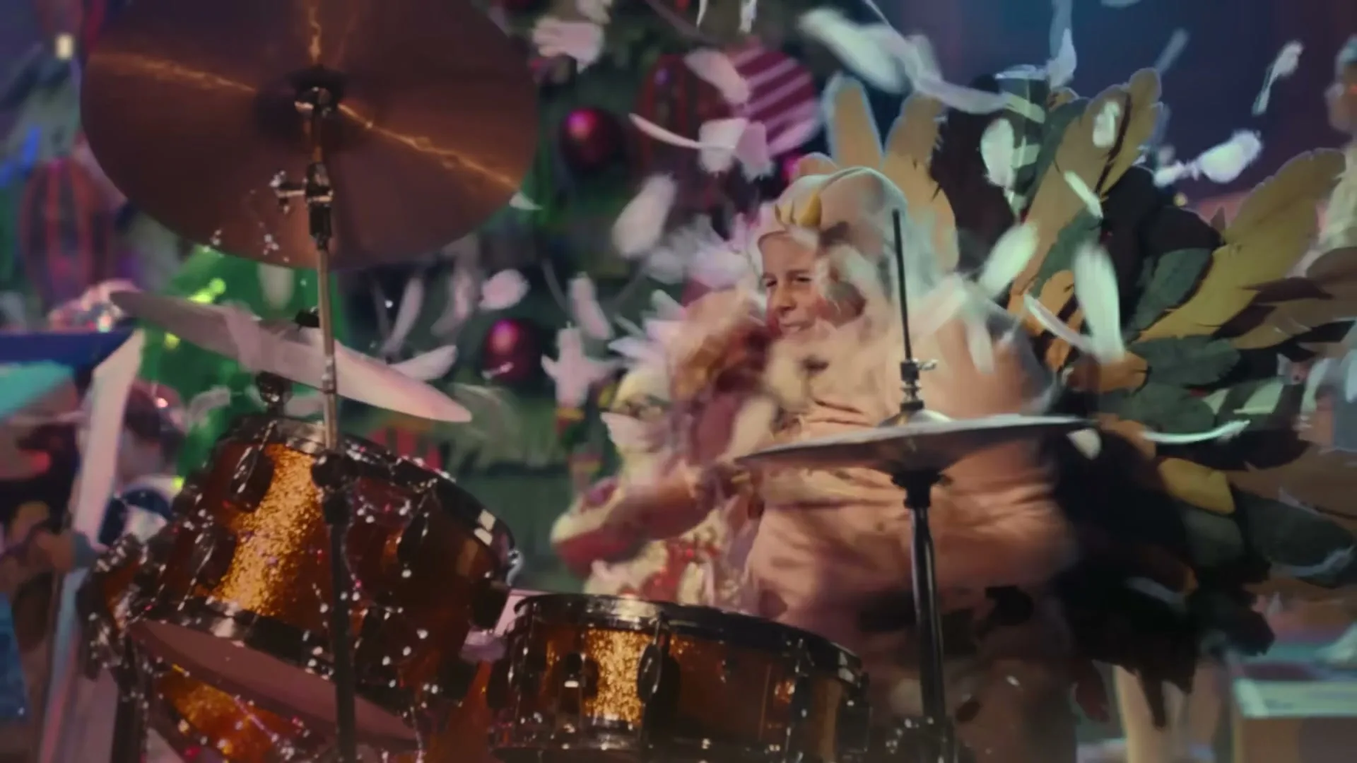 A child dressed as a Christmas turkey plays the drums as feathers fall around them on a festive stage.