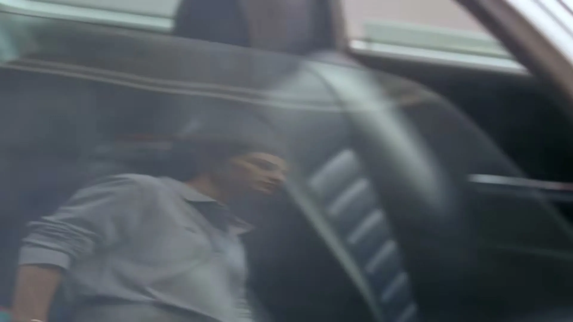 A man in a light blue polo shirt is reflected in a car window, looking out as the car moves.