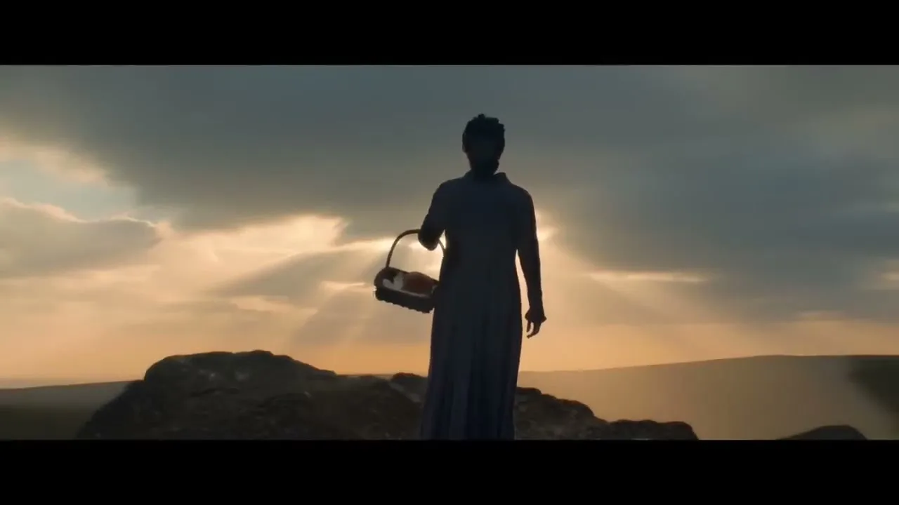 A woman in a long dress, silhouetted against a dramatic sky, stands on a rocky outcrop holding a basket of bread.