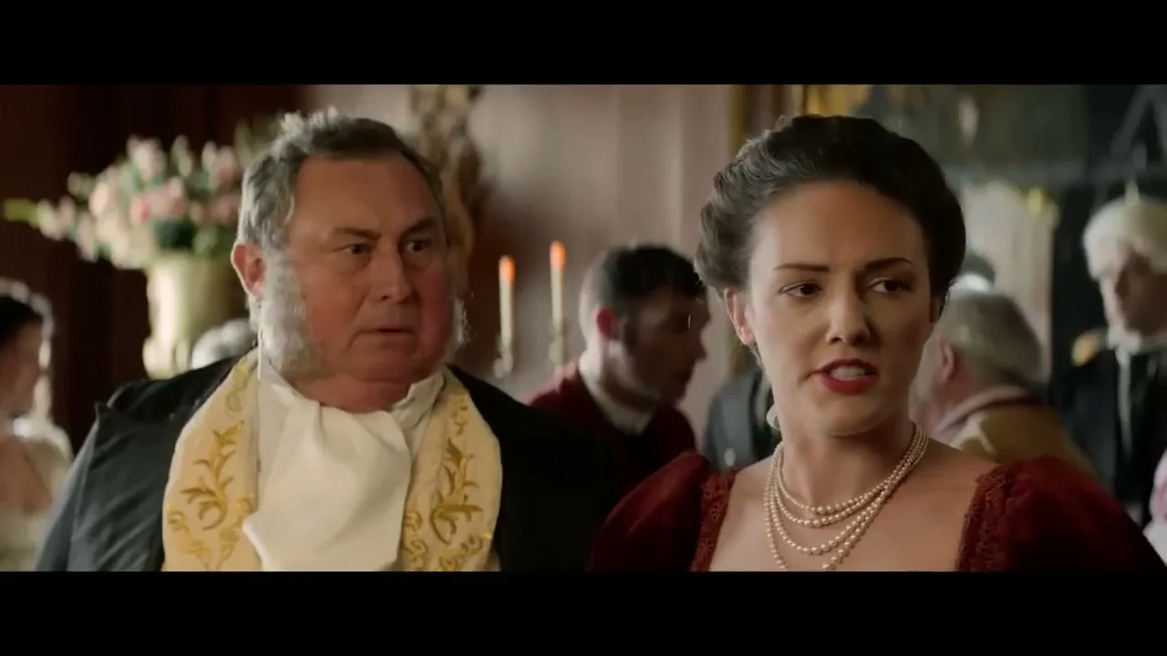 A man with sideburns and a woman in a red dress and pearls look surprised as a woman walks past them at a formal gathering.