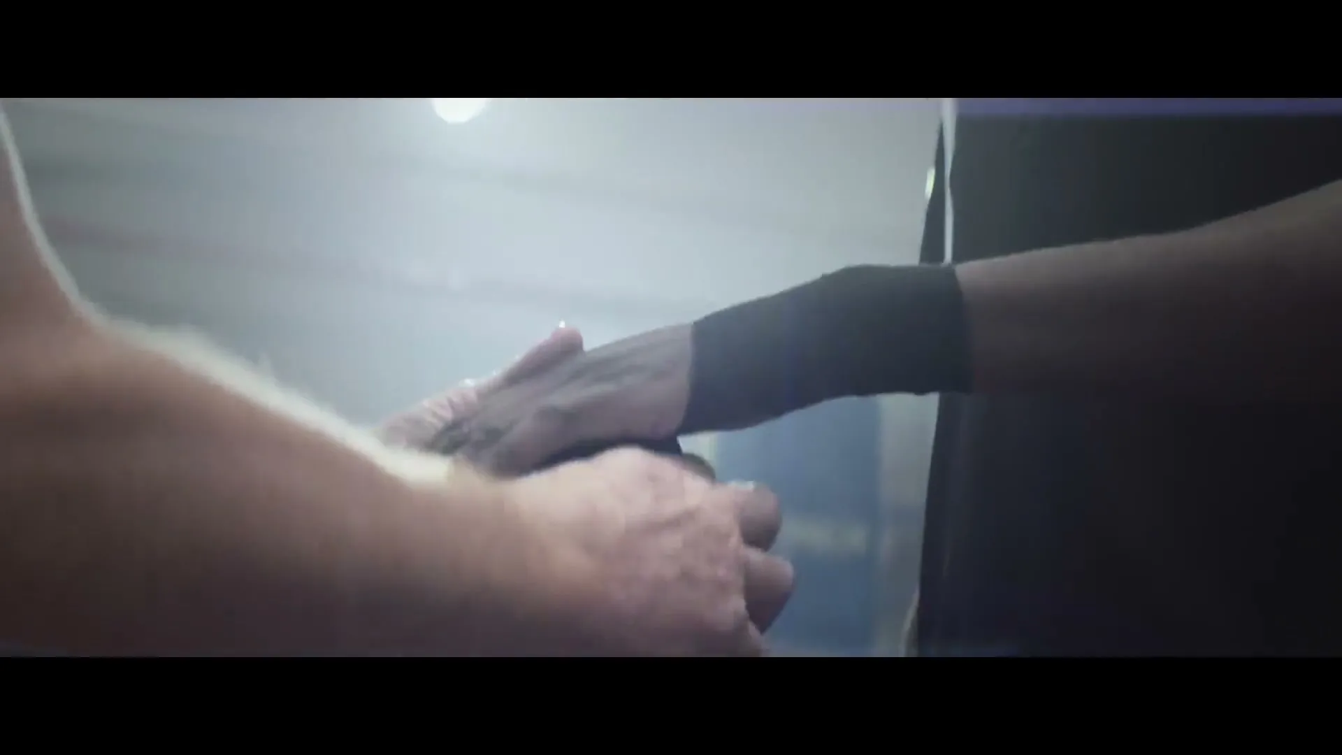 A boxing coach with fair skin wraps the hand of a boxer with dark skin, preparing him for a fight in a dimly lit gym.