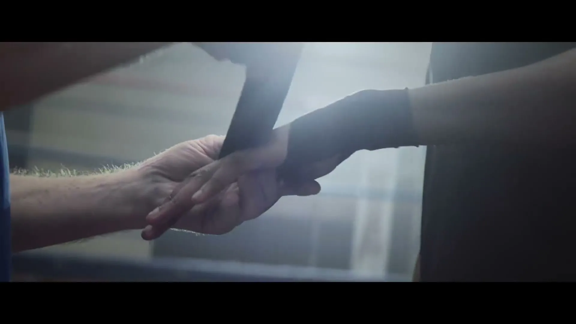 A boxing coach wraps the hand of a boxer in a dimly lit boxing gym, preparing him for training.