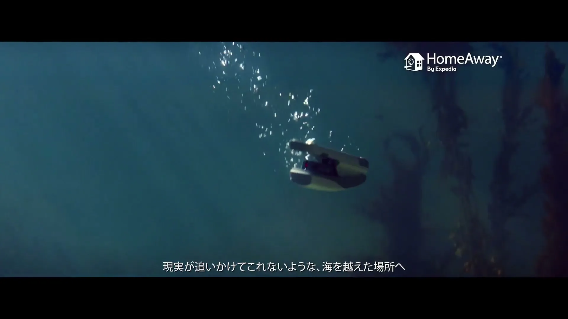 An underwater drone with bubbles above it swims through clear blue water with dark seaweed in the background.