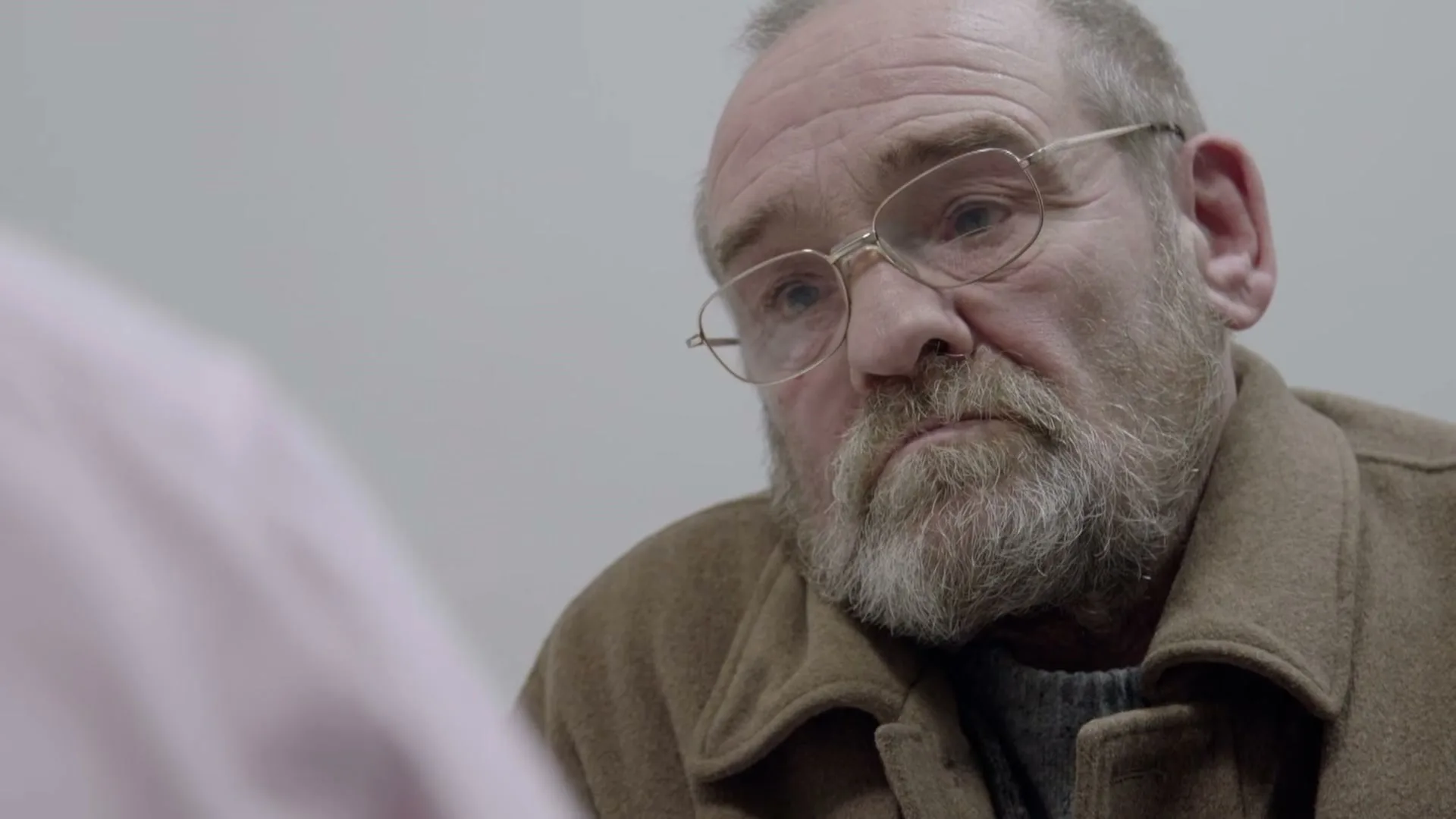 A man with a beard and glasses listens intently, then closes his eyes, in a medical setting.