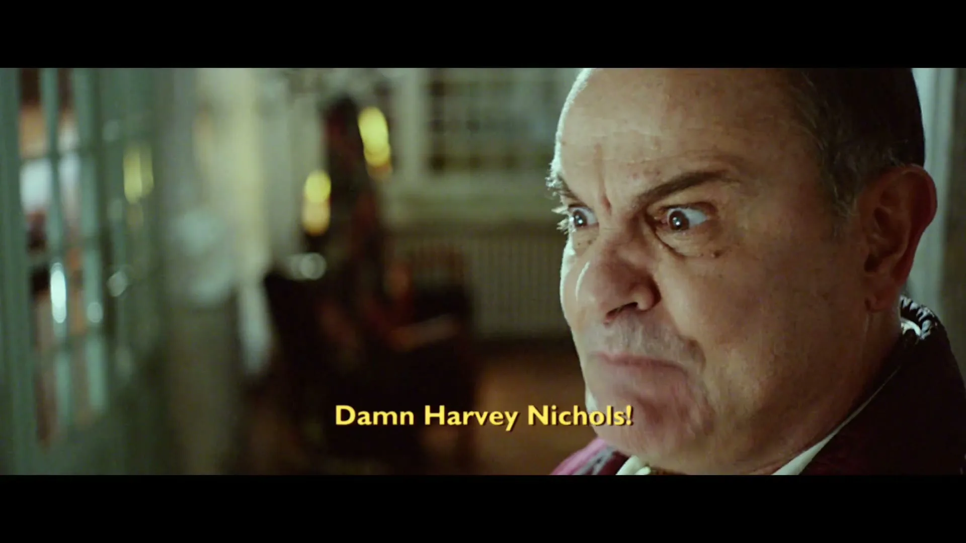 A man in a red robe looks angry and shouts, then turns his back to the camera, in a dimly lit interior.