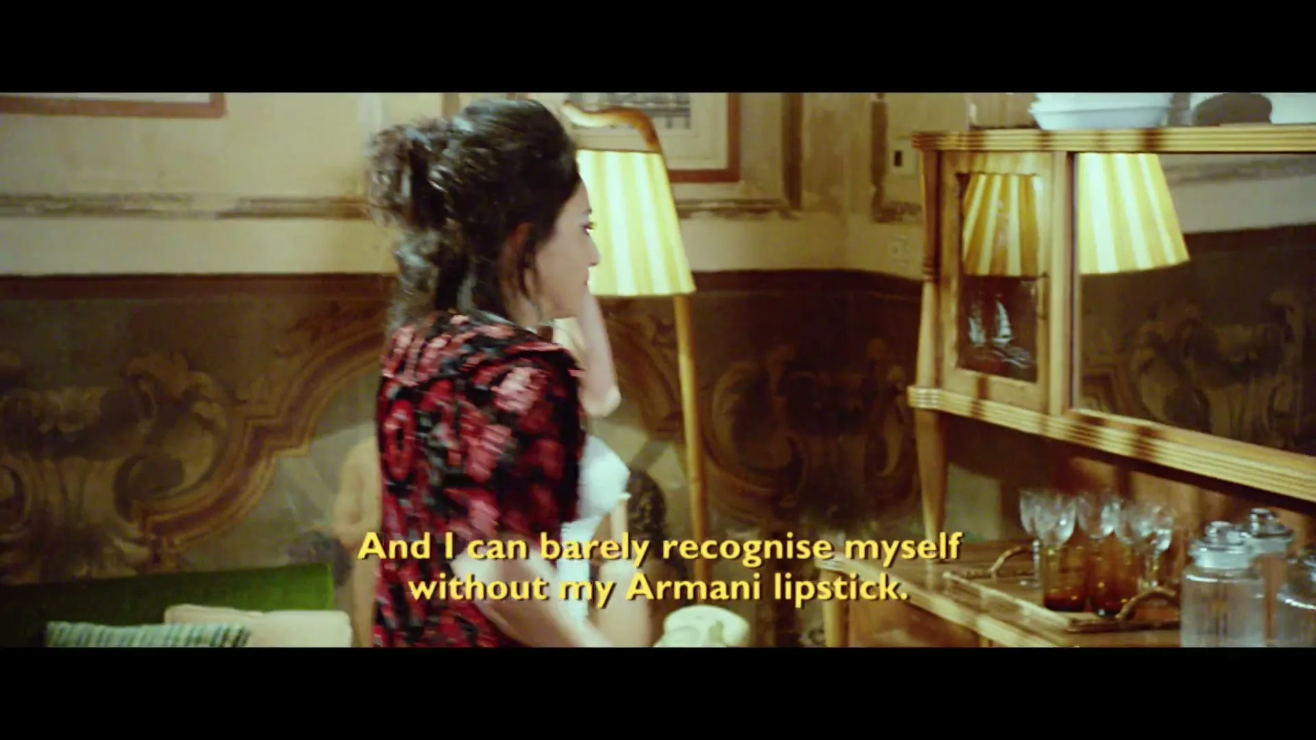 A man in a red robe argues with a woman in a floral top, while another man watches from behind in a lavish interior.
