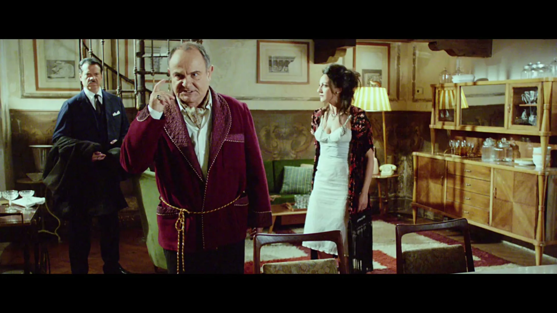 A man in a red robe gestures angrily while two other people stand in a lavish Italian living room, with subtitles on screen.
