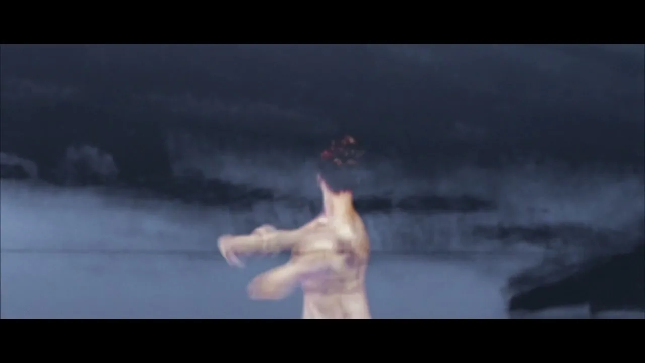 A female ballet dancer in a white dress performs on a stage with a dark, cloudy background, moving gracefully with her arms raised.