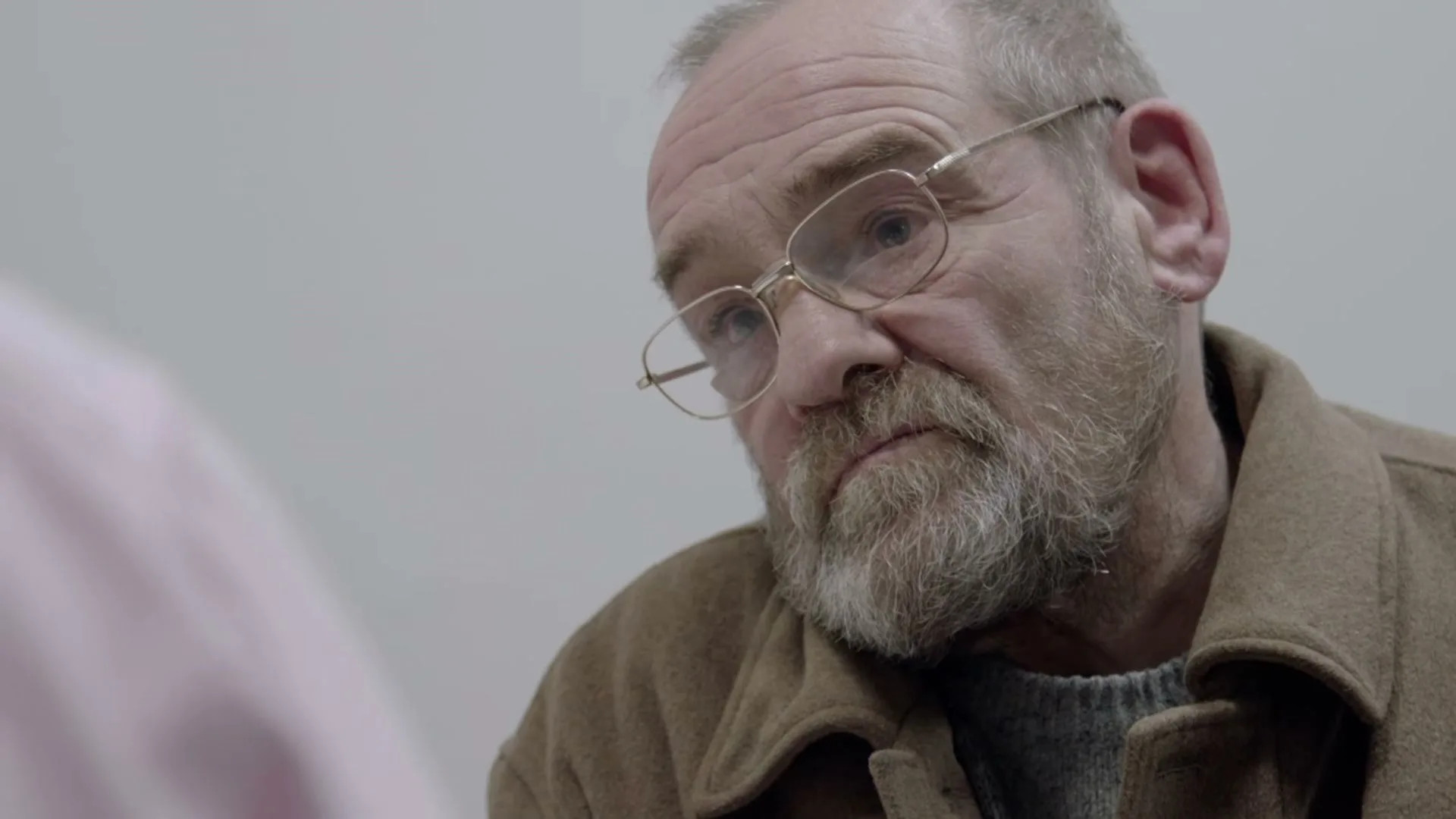 A man with a beard and glasses looks intently at someone off-screen in a medical setting.