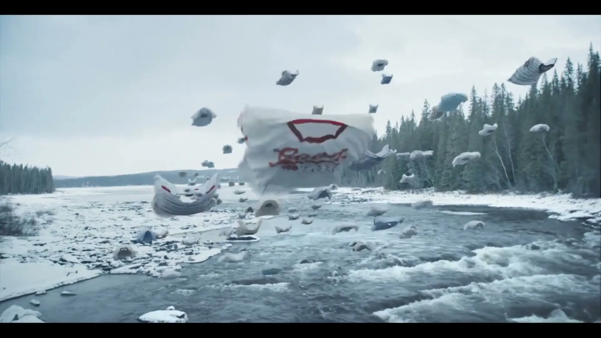 A wide shot shows a snowy river landscape with a forest in the background, as numerous white t-shirts float and tumble through the air above the water.