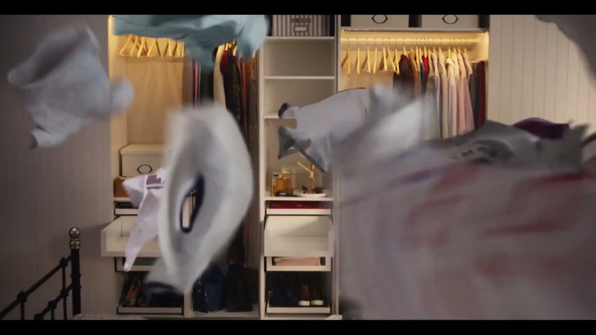 Various clothes, including t-shirts, fly through the air in a bedroom with an open closet in the background.