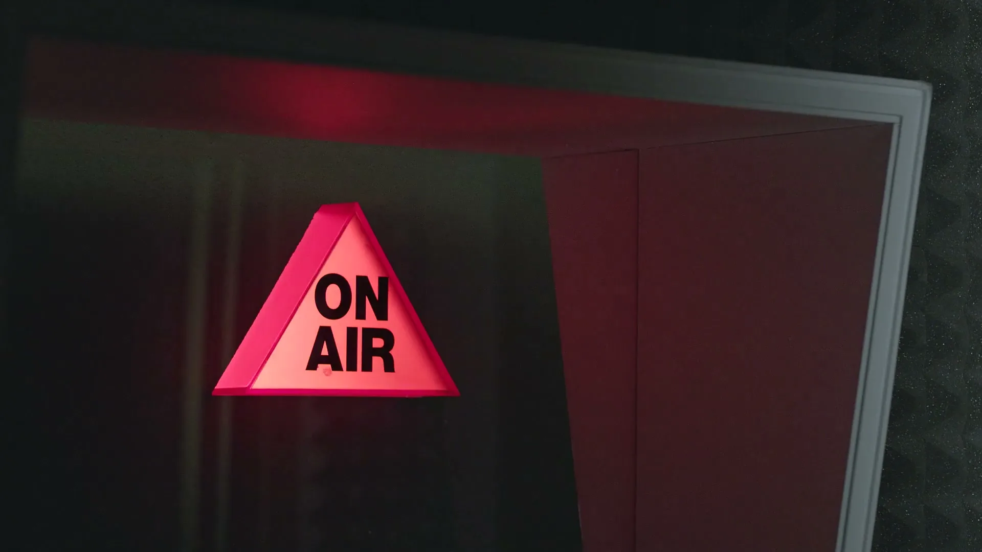 A red triangular "ON AIR" sign illuminates in a dark studio doorway, signaling a broadcast is live.