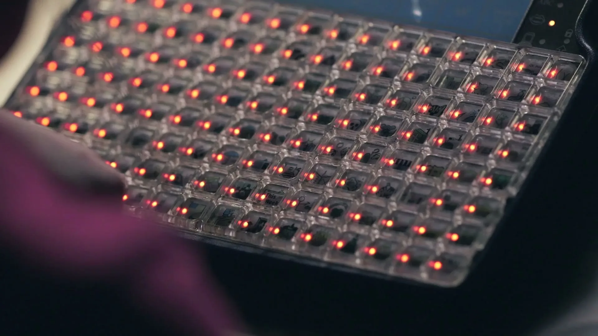 A person's finger presses a button on a transparent keyboard with red lights, in a close-up shot.