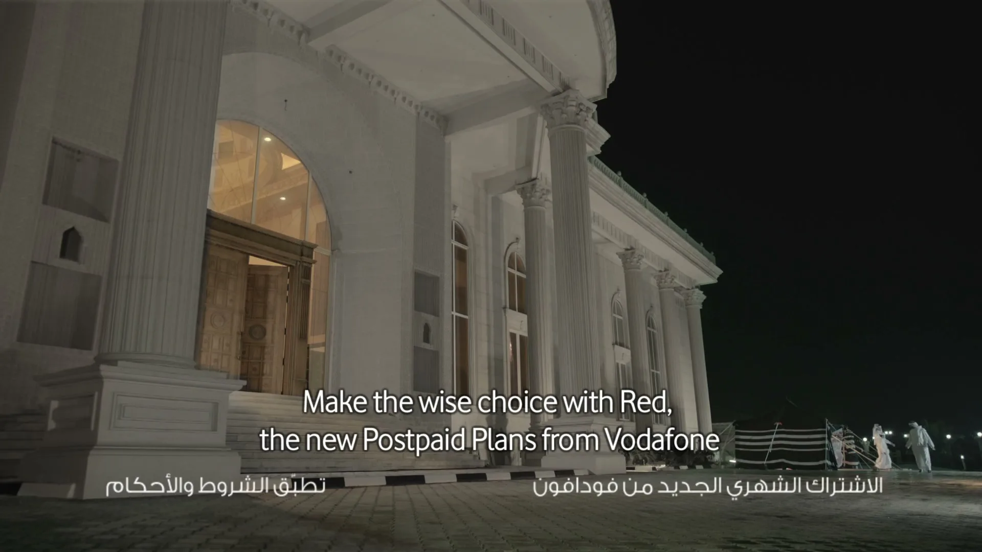 A grand white building with columns and a lit entrance stands at night, with text appearing on screen about Vodafone's new postpaid plans.