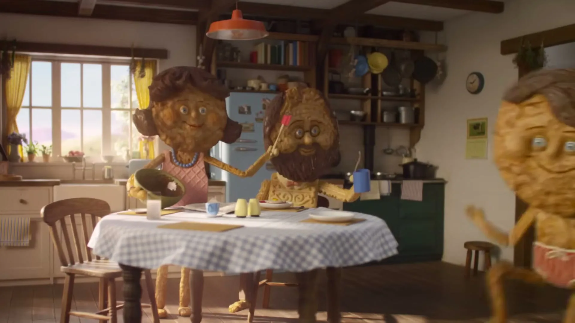 Two biscuit-like characters, a mother and father, stand in a rustic kitchen, as a third biscuit-like character, a child, runs past them.