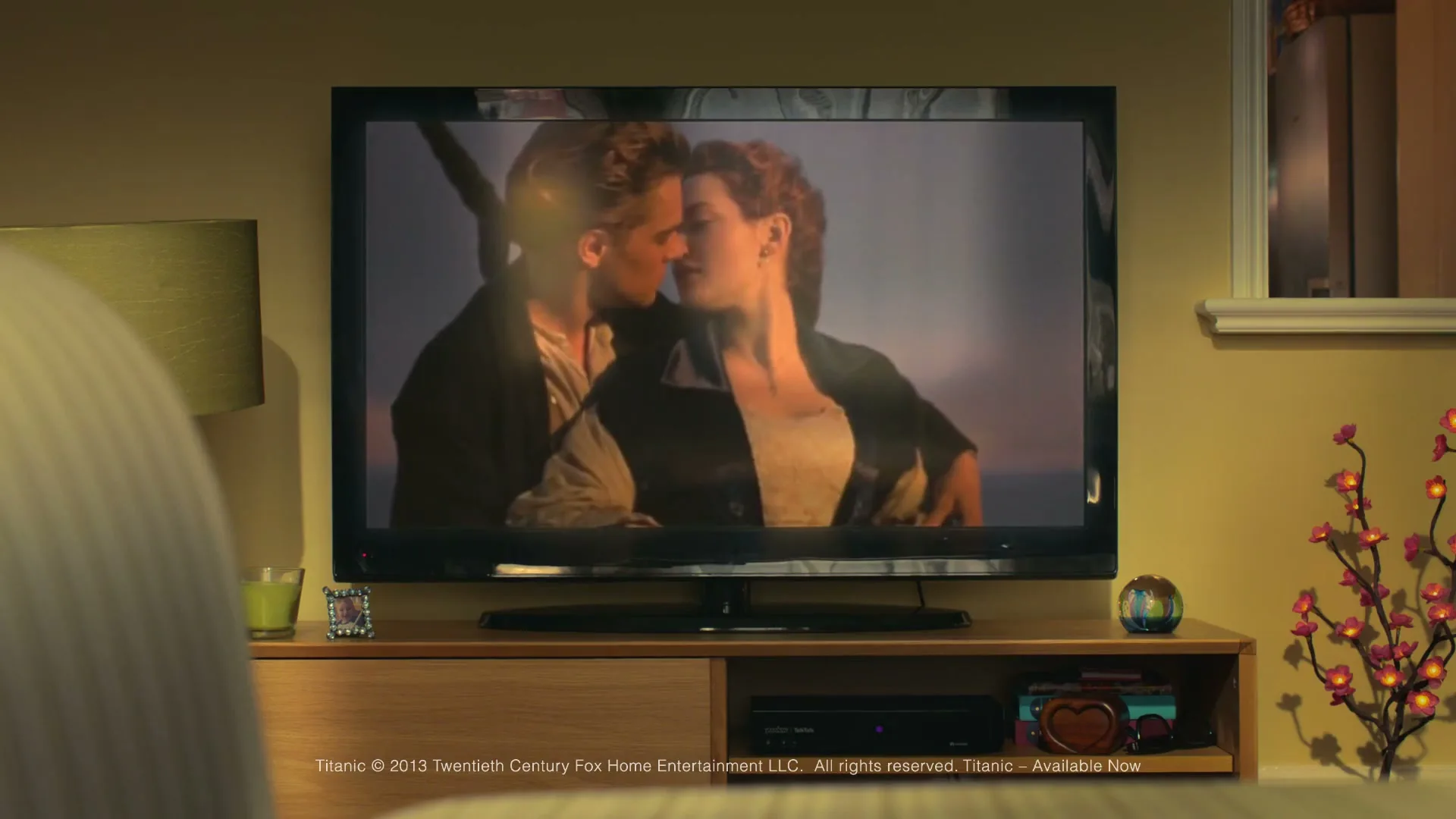 A TV screen shows a romantic scene from the movie Titanic, with Leonardo DiCaprio and Kate Winslet embracing, in a cozy living room at night.