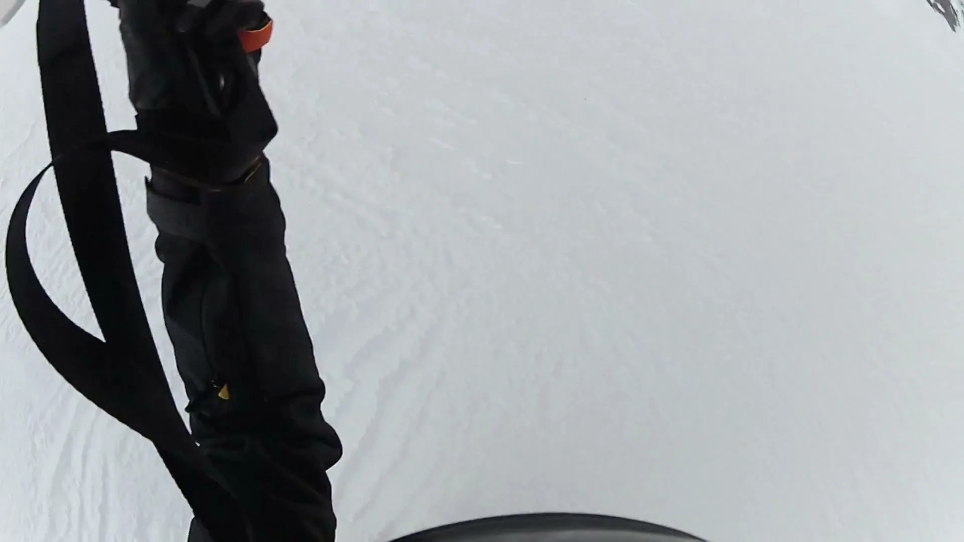 A person's legs in black ski pants and boots are seen from a high angle, walking on a snow-covered surface.