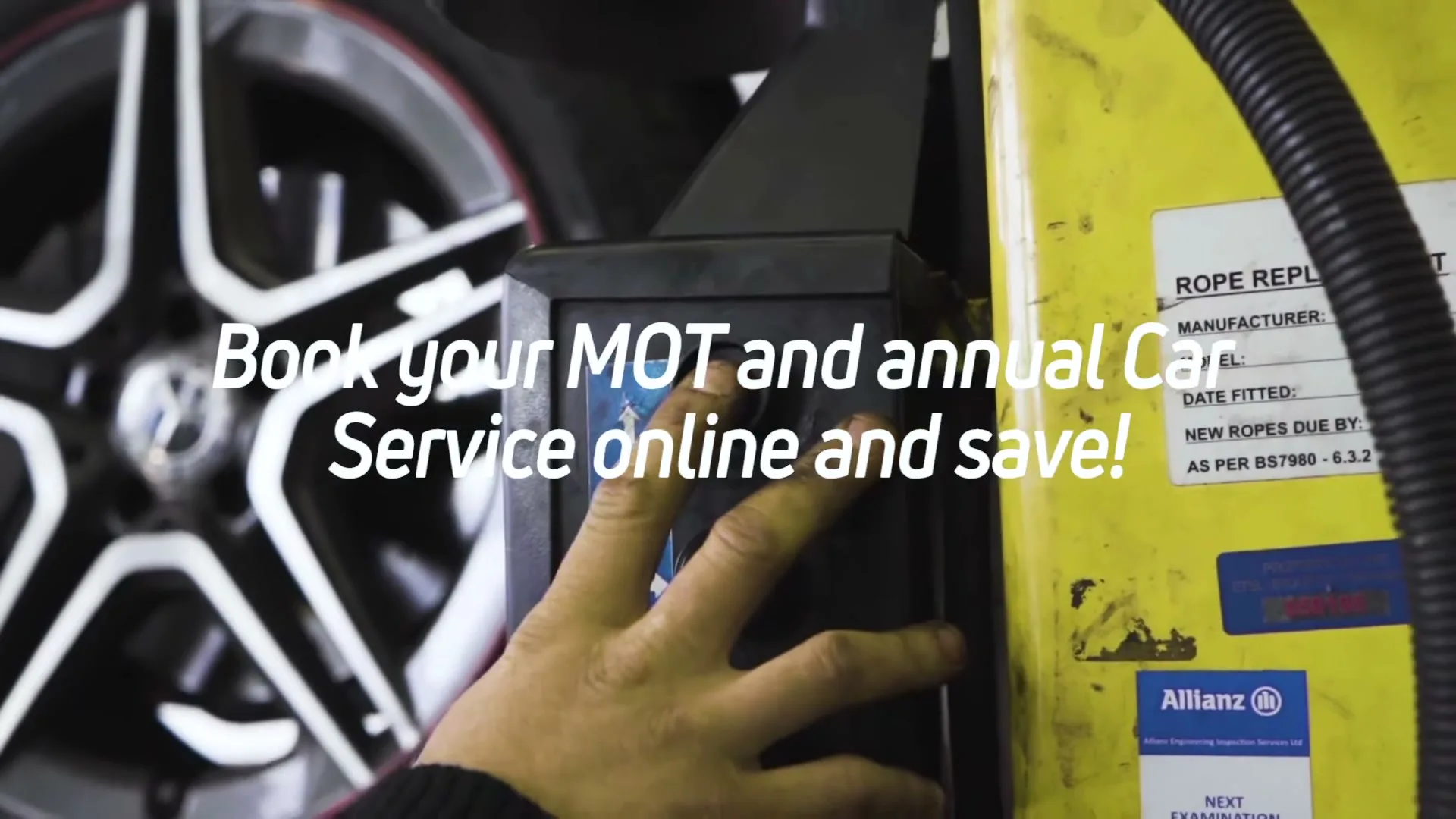 A person's hand presses a button on a machine in a garage, with a car wheel in the background and text overlaid.