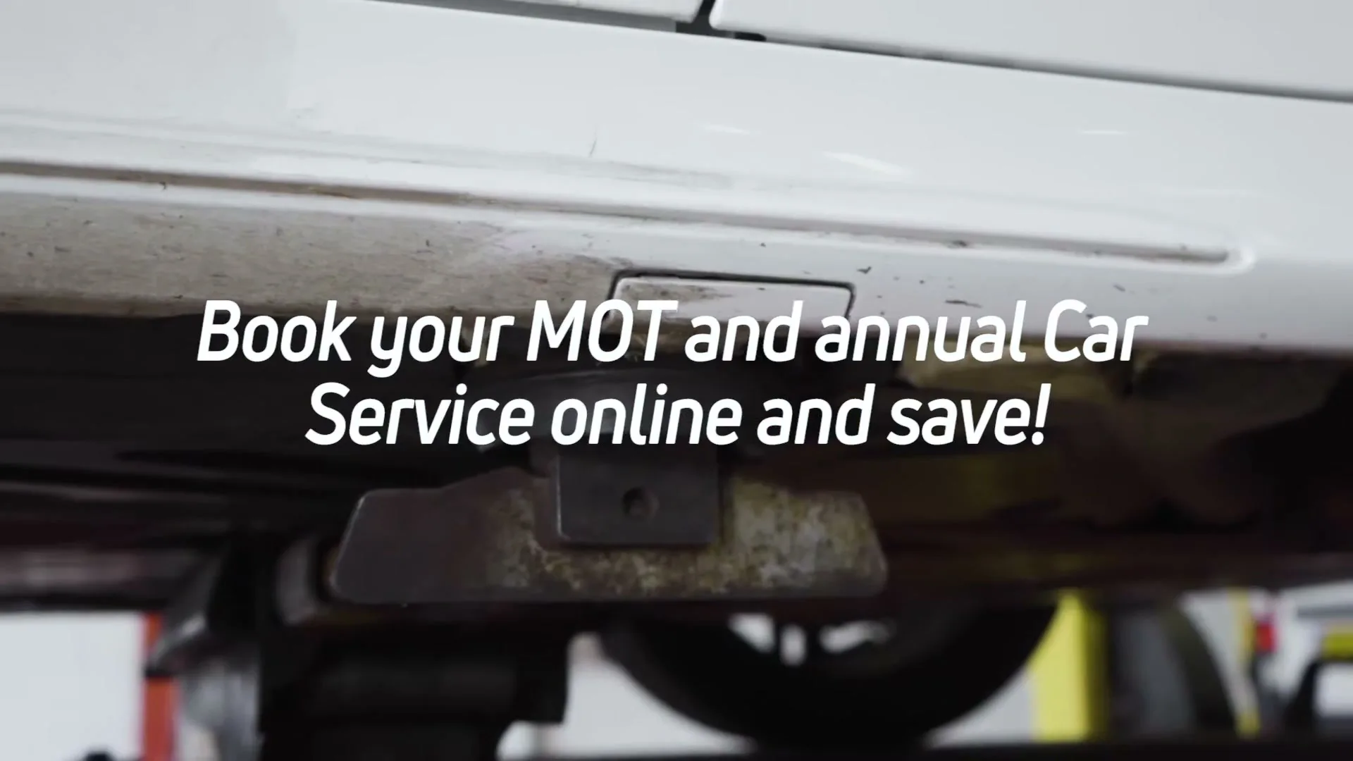 A white car is seen from a low angle, with the undercarriage and a jack visible, as text overlays the screen.