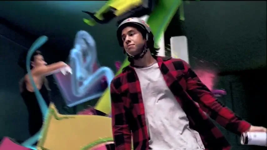 A young man in a helmet and plaid shirt sprays a green stream from a can, surrounded by colorful, abstract shapes in a dark, imaginative space.
