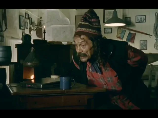 An old man with a mustache and a patterned hat leans over a table, looking intently at something in a rustic interior.