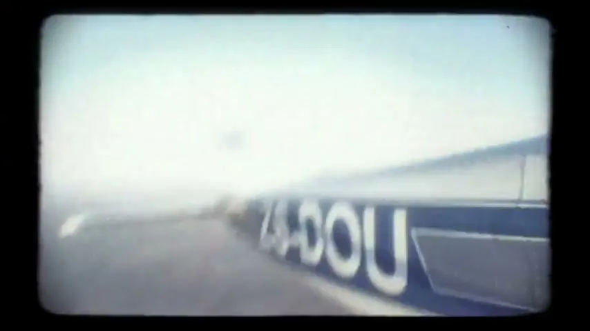 A small plane with blue and white markings flies over a vast, dry landscape under a clear blue sky.