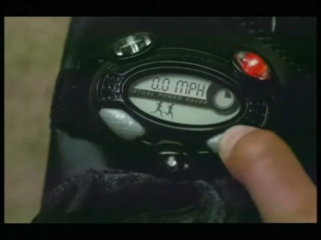 A person's fingers press buttons on a black electronic device with a screen displaying "0.0 MPH" and running figures.