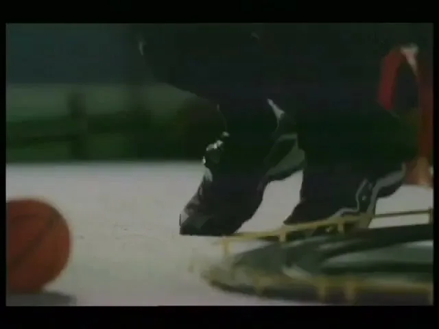 A child's feet in black sneakers step over a toy train track on a light-colored floor, with a basketball nearby.