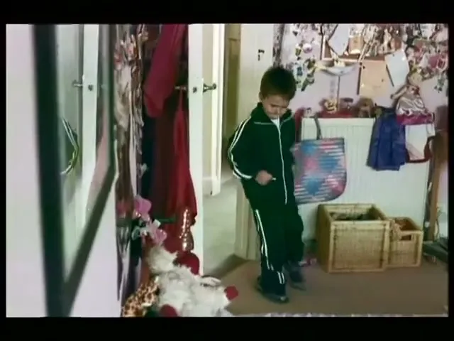 A young boy in a tracksuit runs in place in a sunlit hallway, looking down at his feet.