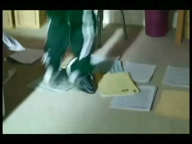 A young boy in a green tracksuit and sneakers runs in place on papers scattered across his bedroom floor.