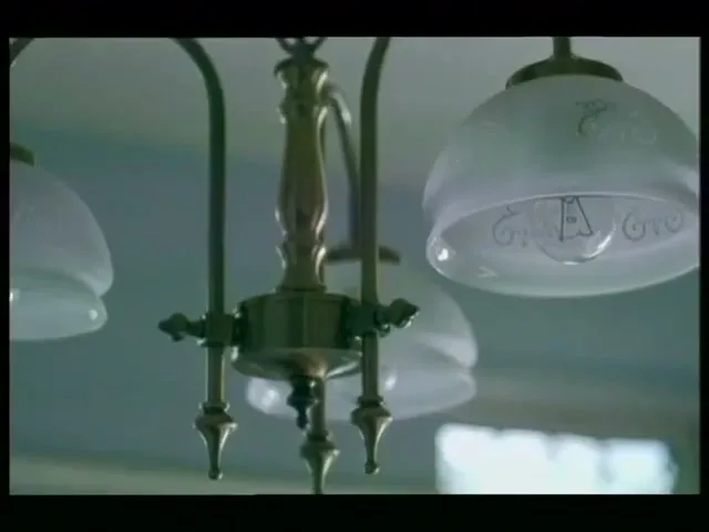A close-up shot of a brass chandelier with frosted glass shades, hanging from a white ceiling in an interior setting.