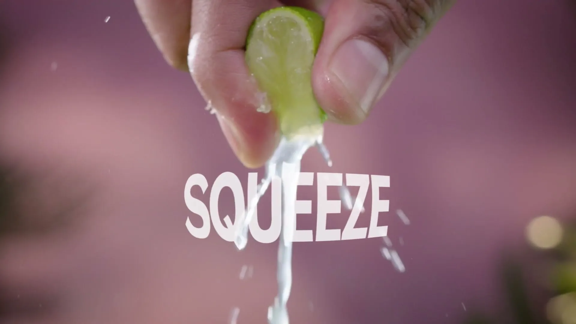 A hand squeezes a lime, with juice and pulp splashing downwards, against a blurred purple background with the word "SQUEEZE" in white text.