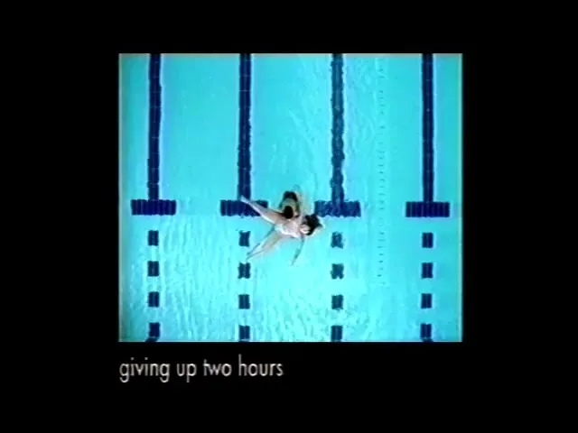 Two female synchronized swimmers in black swimsuits perform a routine in a bright blue swimming pool, viewed from directly above.