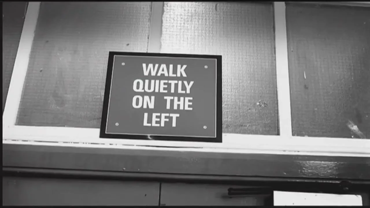 A black and white shot shows a sign on a window that reads "WALK QUIETLY ON THE LEFT" in a school hallway.