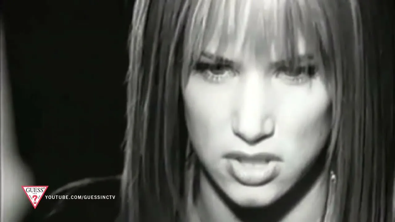 A young woman with long hair and bangs looks intensely at the camera, her mouth slightly open, in a black and white shot.