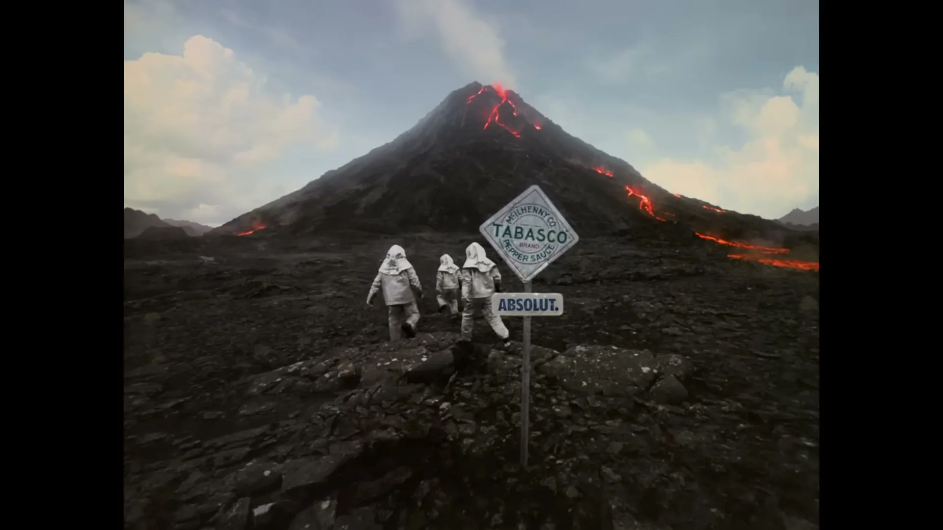 Three people in silver protective suits walk away from the camera towards a smoking volcano with lava flows, passing a sign for Tabasco and Absolut.
