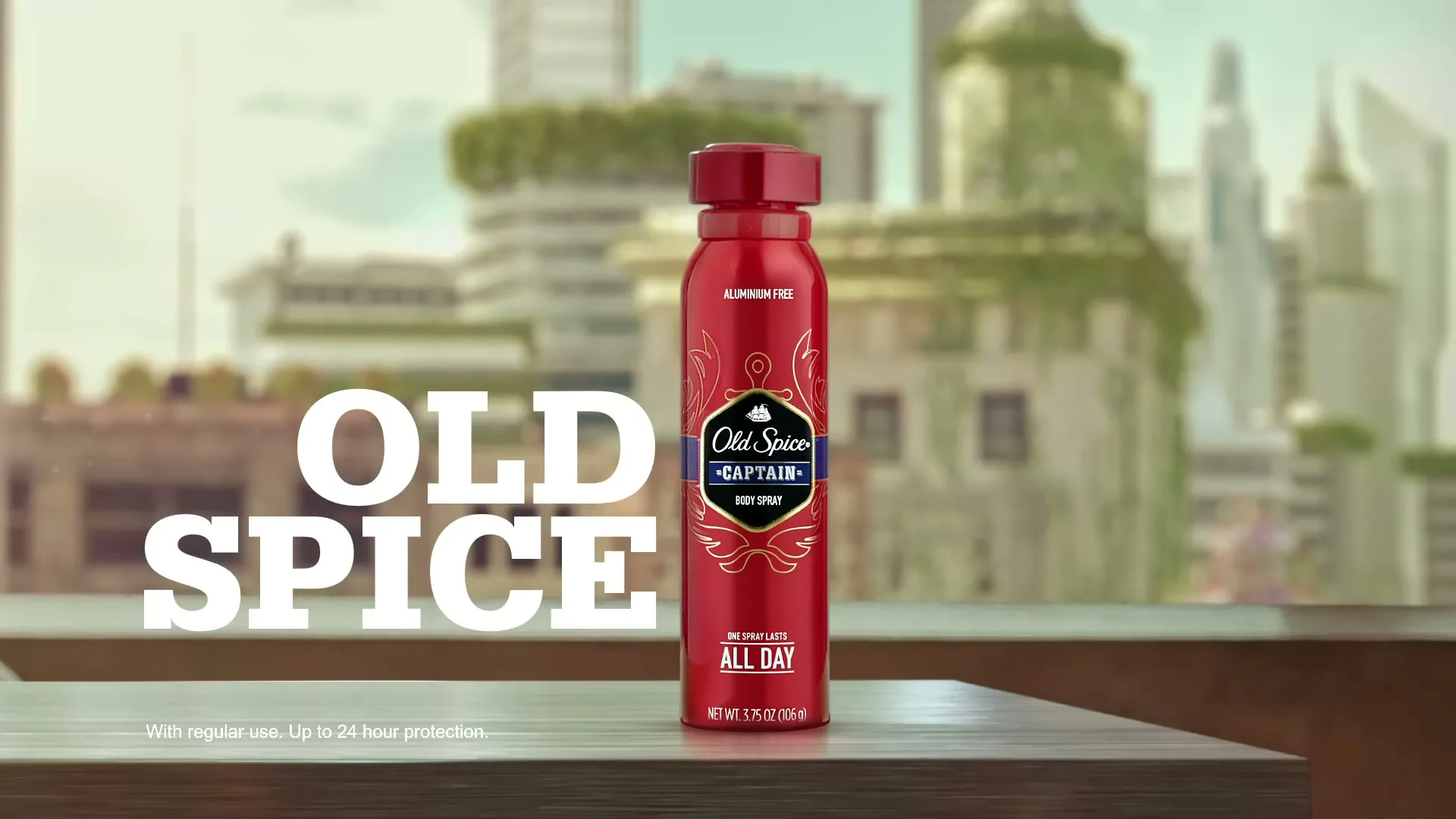 A red Old Spice Captain body spray can sits on a wooden surface with a blurred city skyline in the background, as a hand reaches in to grab it.