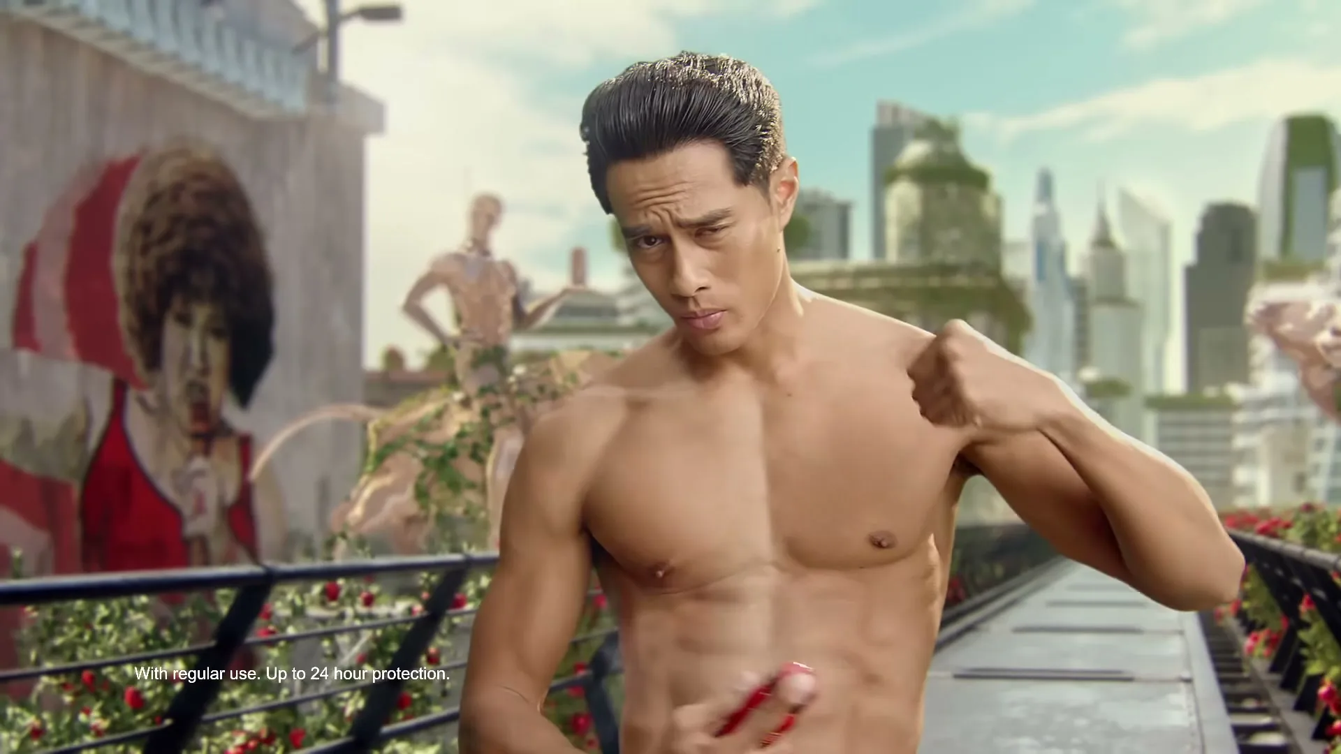A shirtless man with dark hair flexes his bicep and sprays deodorant on his chest, looking at the camera with a quizzical expression on a futuristic bridge.