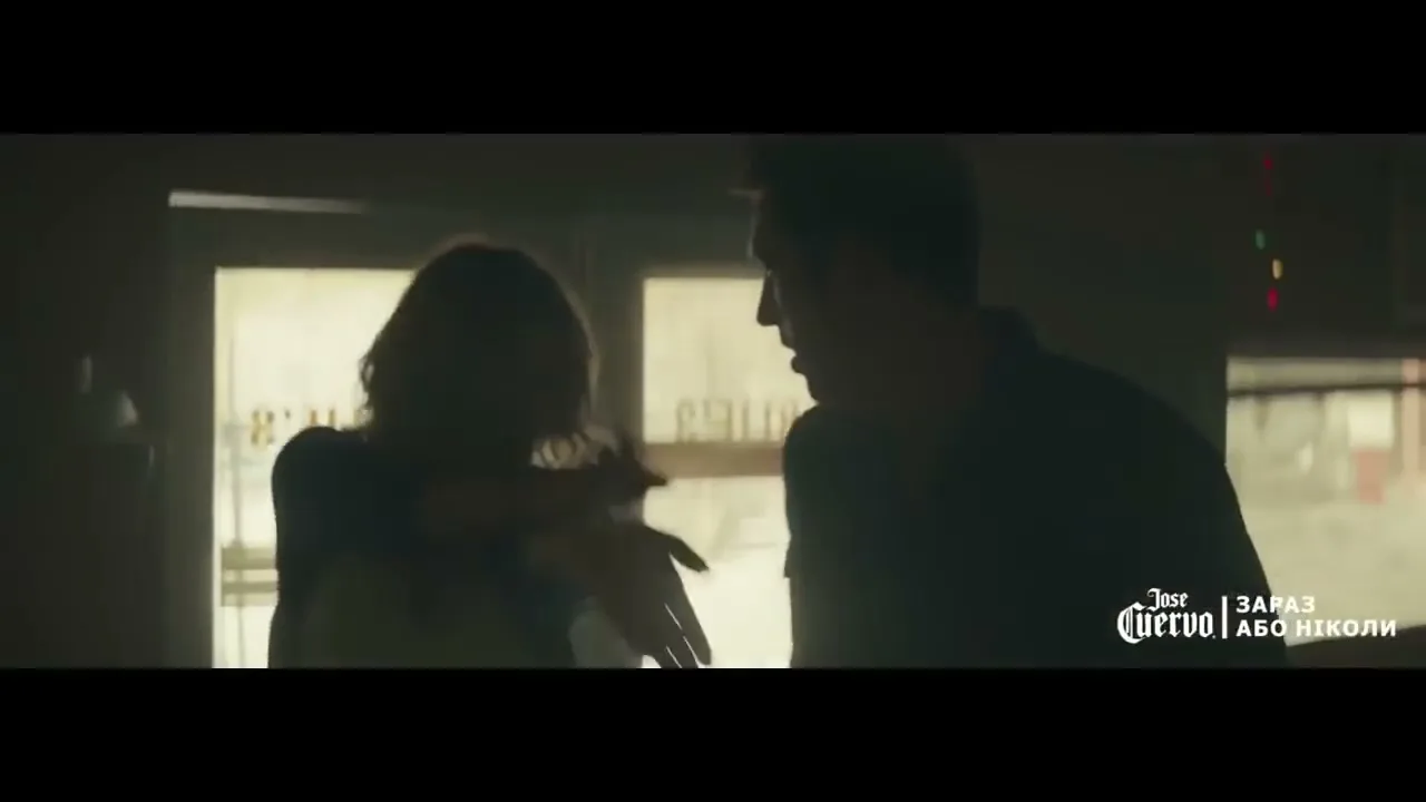 A man and woman dance closely in a dimly lit bar, silhouetted against a bright window.