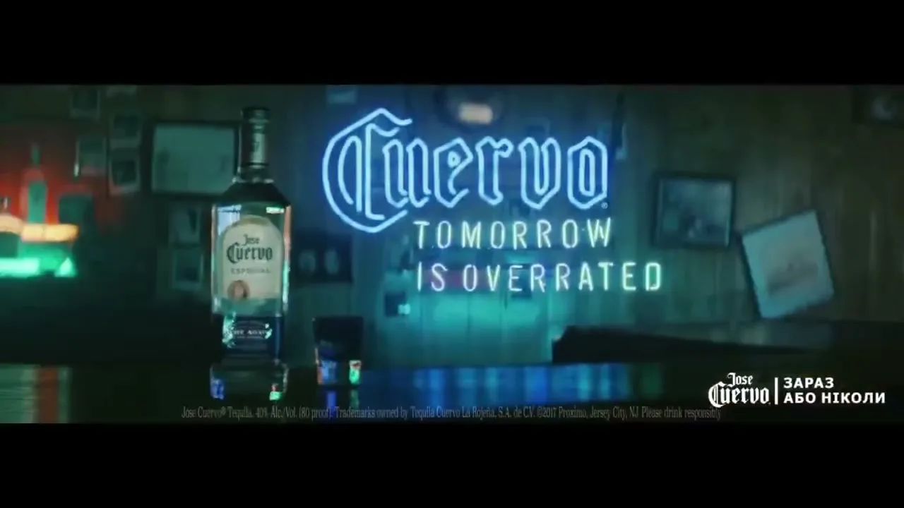 A bottle of Jose Cuervo tequila and two shot glasses sit on a bar counter, with a neon sign in the background that reads "Cuervo Tomorrow is Overrated."