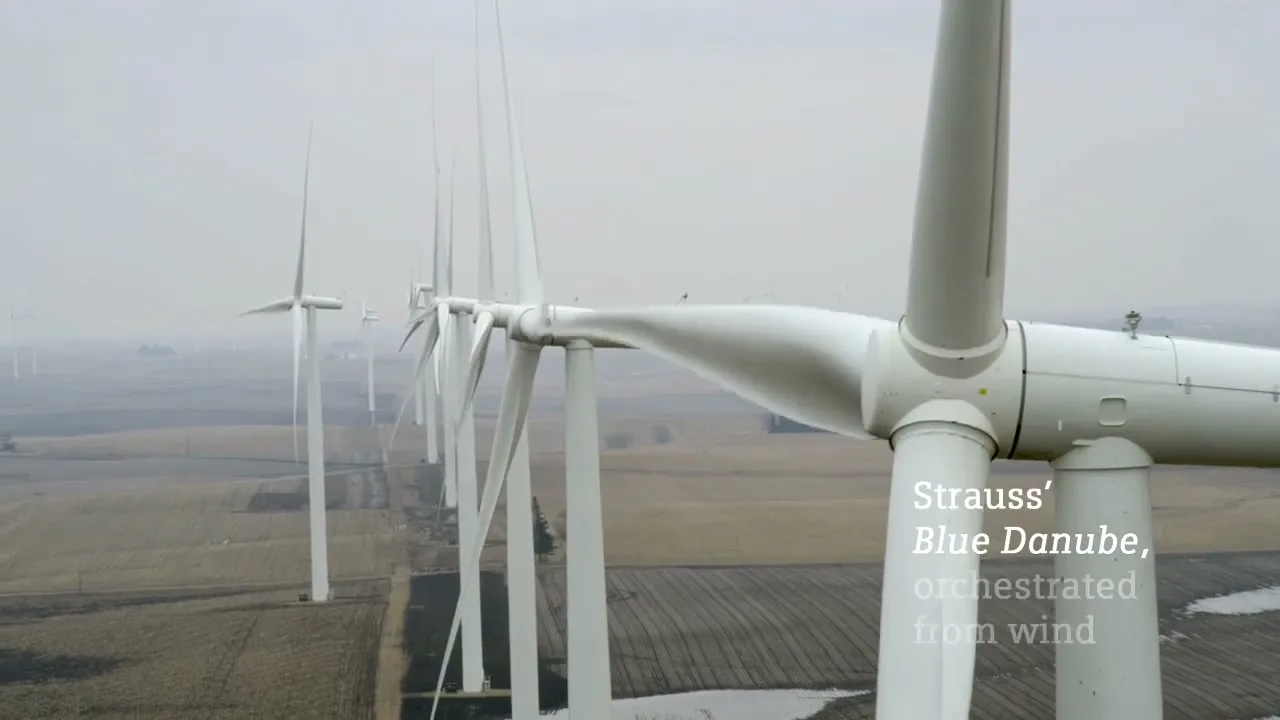 A line of white wind turbines stands tall in a vast, flat landscape under a cloudy sky, with text overlayed on the right side.