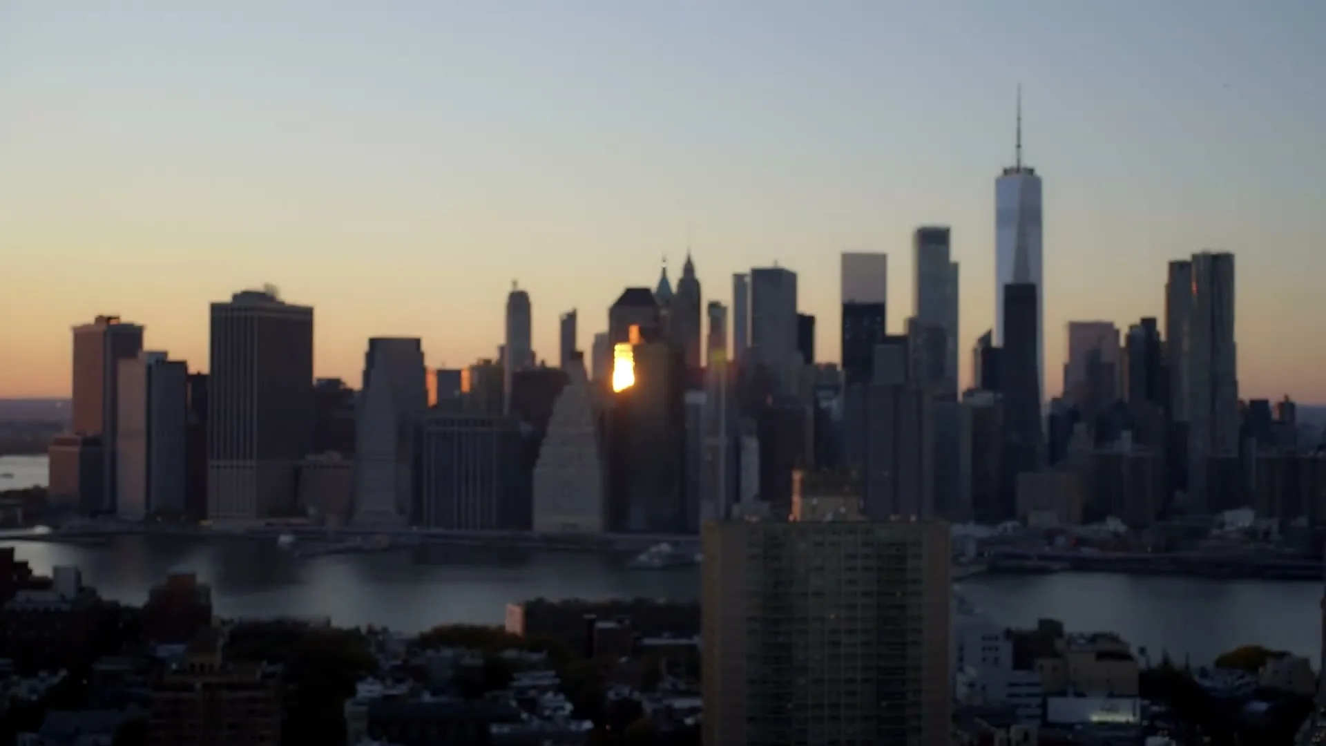 An establishing shot of the New York City skyline at sunset, with the sun reflecting off a building, as the camera racks focus from blurry to sharp.