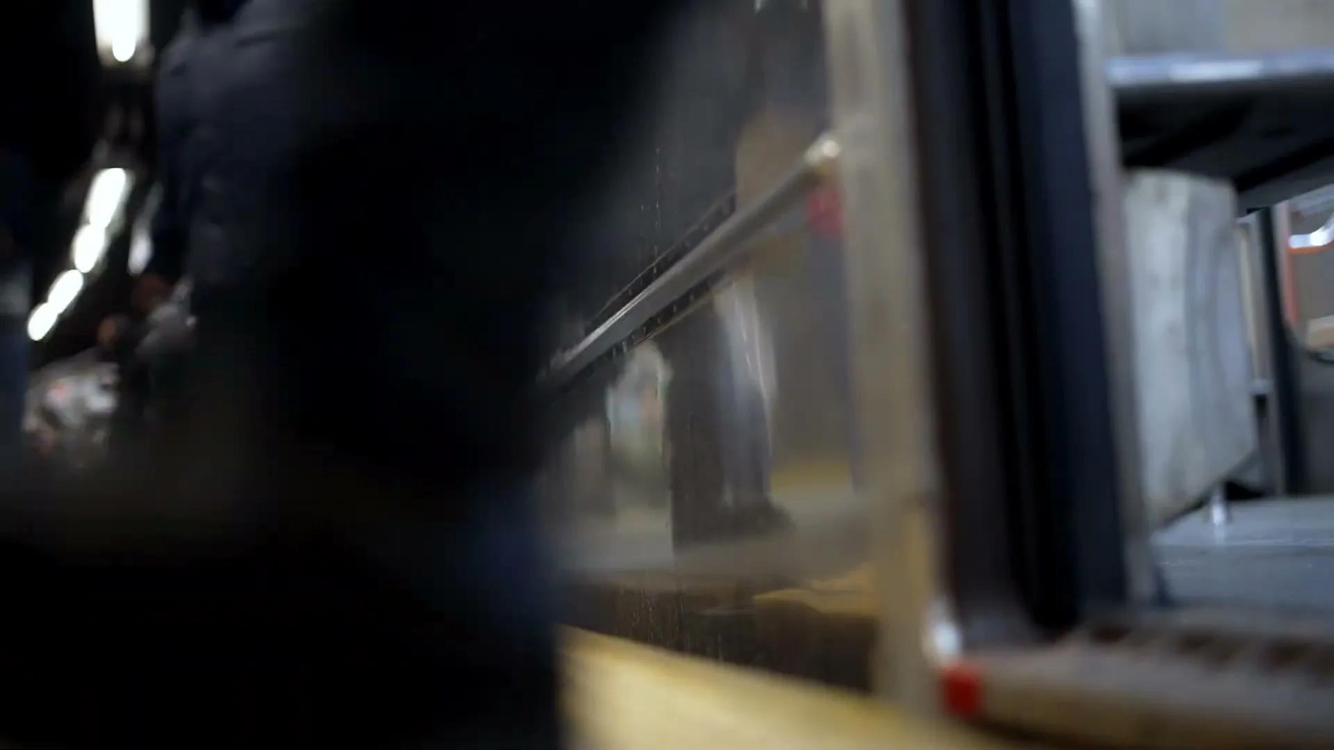 A low-angle shot shows people's legs as they board a subway train at a station platform, with the train doors open.